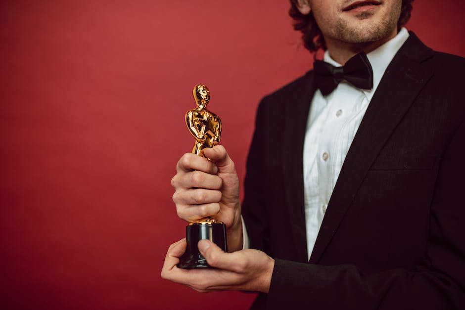 A group of celebrities at an awards show, some holding trophies, with paparazzi and cameras flashing in the background.