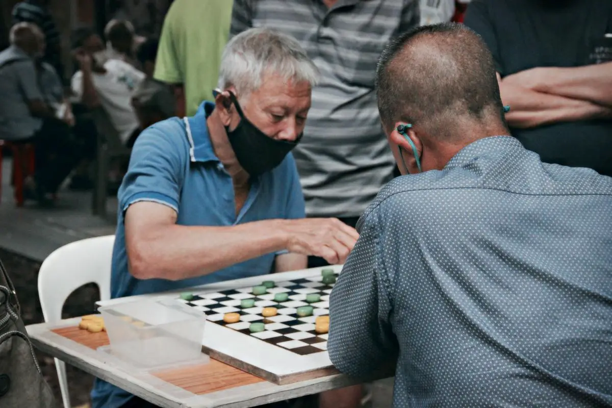 A group of people sitting around a table playing chess and talking, representing the social interaction and competition in a chess club