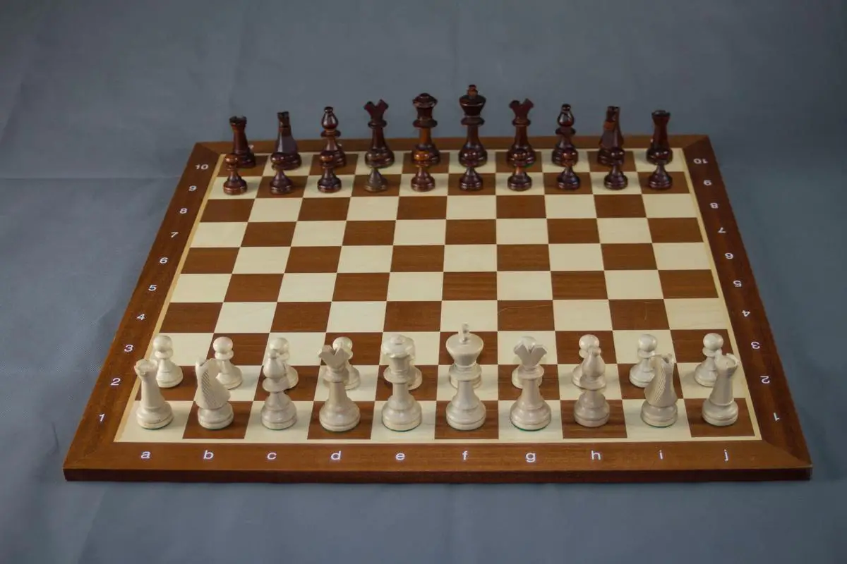 A chess board with pieces set up and a hand hovering over them, representing the coaching and guidance that players can receive in chess coaching.