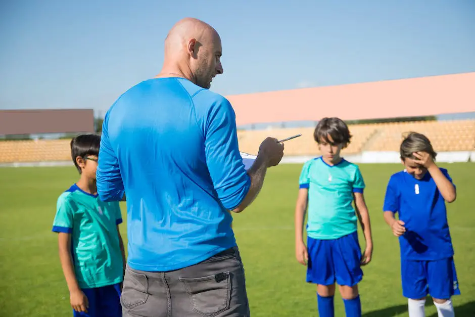 A group of children playing football in a field, with a coach watching them. The coach is holding a clipboard and looks engaged with the game, while the children are all smiling and having fun.
